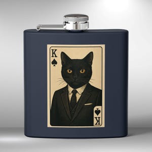 May include: A black stainless steel hip flask with a silver cap. The flask features a sticker of a black cat wearing a suit and tie. The cat is holding a playing card that says "K" for King of Spades.