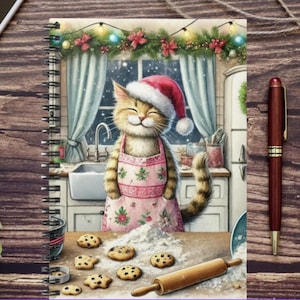 Puede incluir: Cuaderno de espiral con una ilustración de un gato sonriente con gorro de Papá Noel y delantal, horneando galletas en una cocina. La portada presenta un rodillo, galletas y un tema navideño.