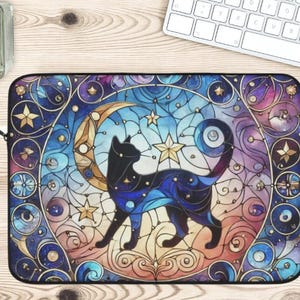 Könnte beinhalten: Eine Laptoptasche mit einem Buntglasdesign, das eine schwarze Katze vor einem Halbmond und Sternen zeigt. Der Hintergrund ist eine lebendige Mischung aus Blau, Lila und Gold.