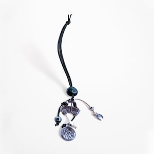 Puede incluir: Un cordón de cuero negro con un dije de plata de un coche, una herradura y un dije redondo con un diseño. El cordón tiene una cuenta verde oscuro.
