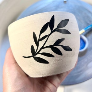 May include: A white ceramic planter with a black silhouette of a leafy branch design.