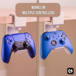 May include: A white under-desk controller mount with a screw-tightening mechanism, holding a blue PlayStation controller on the left and a blue Xbox controller on the right. The text "WORKS ON MULTIPLE CONTROLLERS" is displayed at the top.