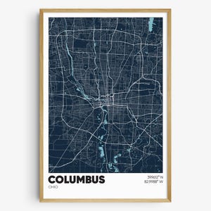 May include: A blue and white map print of Columbus, Ohio. The map shows the city's streets and waterways. The text "COLUMBUS" and "OHIO" are printed below the map, along with the city's coordinates: 39.9612° N, 82.9988° W.