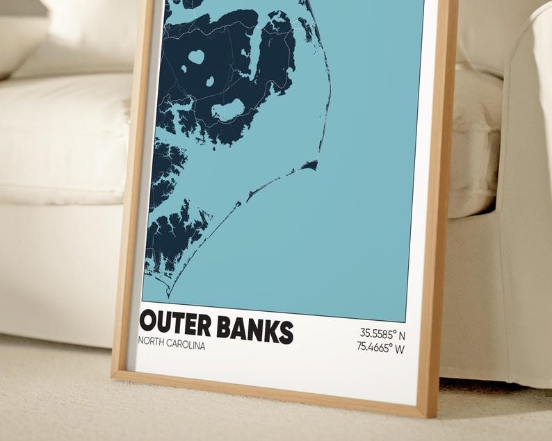 May include: A framed map of the Outer Banks, North Carolina, with a blue and white color scheme. The map shows the coastline and islands of the Outer Banks. The text "Outer Banks" and "North Carolina" is printed below the map, along with the coordinates "35.5585&deg; N, 75.4665&deg; W".