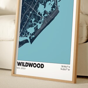 May include: A framed map of Wildwood, New Jersey, with a blue and white color scheme. The map shows the city's streets and waterways. The text "WILDWOOD" and "NEW JERSEY" is printed in black at the bottom of the map. The coordinates "38.9841&deg; N 74.8247&deg; W" are printed in black below the text.