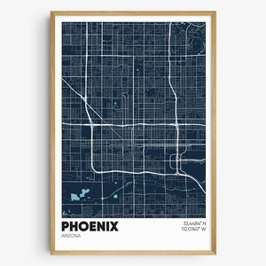 May include: A framed map print of Phoenix, Arizona, featuring a dark blue background with white street grids and highway lines. The text PHOENIX ARIZONA and the coordinates 33.4484 N 112.0740 W are printed in black at the bottom of the white border.