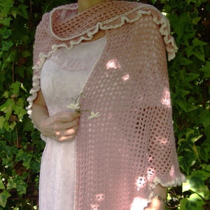 Może przedstawiać: Różowy szal wykonany na szydełku z białymi ozdobami i falowanym brzegiem. Szal jest zarzucony na białą sukienkę z kwiatowym wzorem.