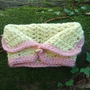 May include: A crocheted baby blanket in yellow and pink with a wooden button in the center.