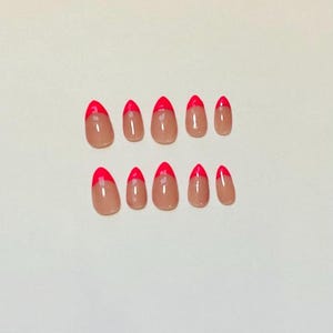 May include: A set of ten oval-shaped false nails. Each nail has a nude base with a bright red French tip. The nails are arranged in two rows of five against a plain white background. The nails are a beauty product.