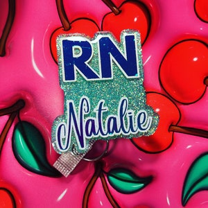 Puede incluir: Una insignia azul y blanca con brillantina con el texto "RN Natalie" sobre un fondo rosa y verde.
