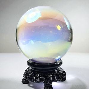 May include: A clear iridescent glass ball on a black ornate stand. The ball reflects light and creates a rainbow effect.