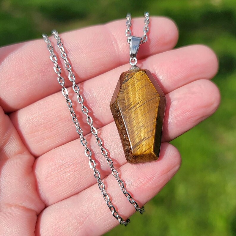 May include: A silver chain necklace with a gold tiger's eye pendant shaped like a coffin.