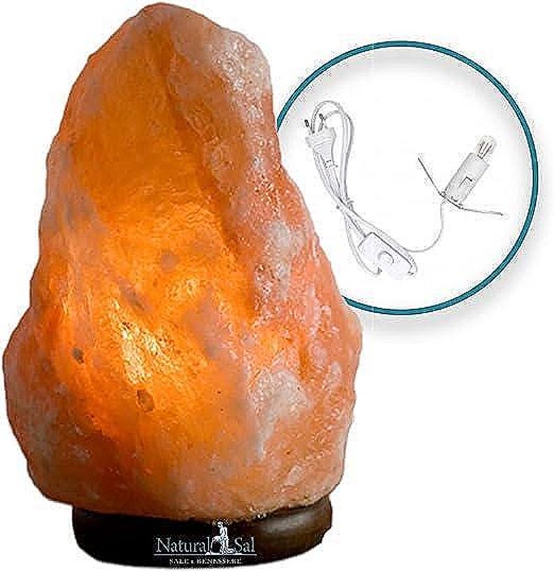 Puede incluir: L&aacute;mpara de sal del Himalaya con una combinaci&oacute;n de colores naranja y blanco. La l&aacute;mpara est&aacute; sobre una base marr&oacute;n oscuro e incluye un cable de alimentaci&oacute;n y una bombilla. La l&aacute;mpara tiene el texto "Natural Sal" en la base.