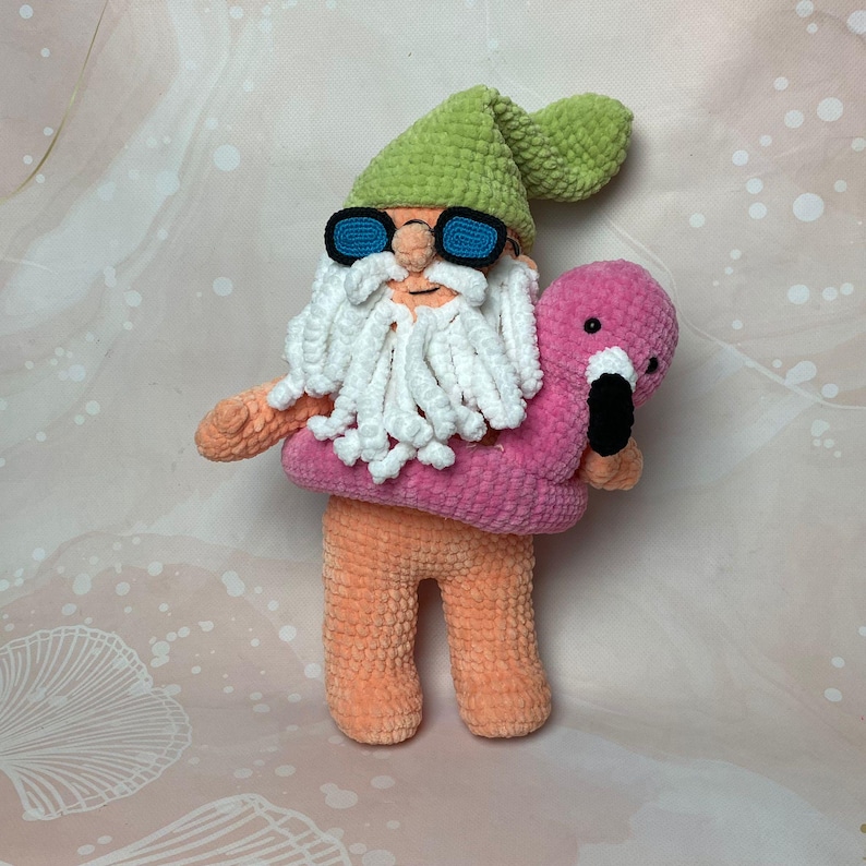 May include: A crocheted gnome wearing green sunglasses and a pink inflatable ring with a pink flamingo in its arms.