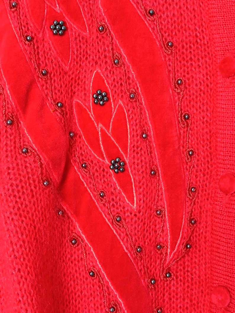 Puede incluir: Su&eacute;ter de punto rojo con un dise&ntilde;o de terciopelo y adornos de cuentas negras.