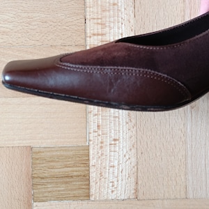 May include: A brown leather and suede heeled shoe with a pointed toe.