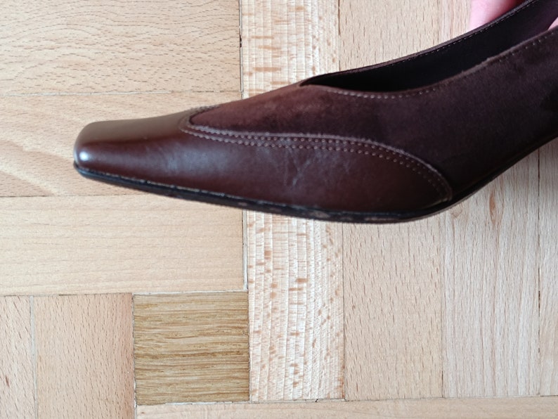May include: A brown leather and suede heeled shoe with a pointed toe.