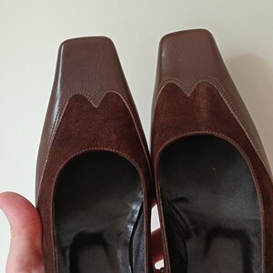 May include: A pair of brown leather heeled shoes with a suede detail on the toe. The shoes have a square toe and a low heel. The brand name "BORAH" is visible on the sole of one shoe.