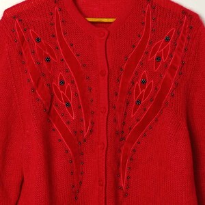 Puede incluir: Un c&aacute;rdigan de punto rojo con un dise&ntilde;o floral de cuentas y terciopelo en la parte delantera.