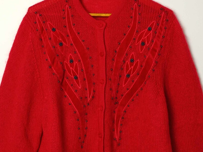 Puede incluir: Un c&aacute;rdigan de punto rojo con un dise&ntilde;o floral de cuentas y terciopelo en la parte delantera.