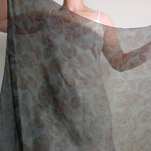 Puede incluir: Un pañuelo rectangular y transparente con un patrón repetitivo de hojas de color marrón y óxido sobre un fondo verde salvia translúcido y apagado. La tela ligera tiene una calidad suave y semitransparente con bordes acabados.