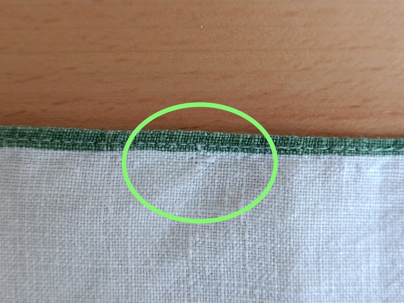 May include: Close-up of a white fabric with a green stitched border. The stitching is visible in the center of the image.