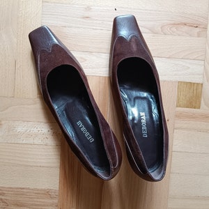 May include: A pair of brown suede heeled shoes with a square toe. The shoes have the word "DEBORAH" written on the inside of each shoe.