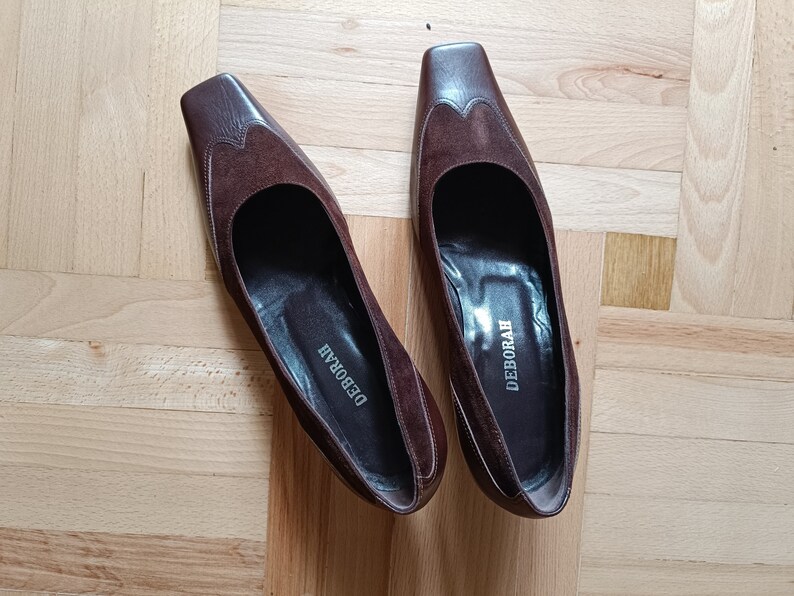 May include: A pair of brown suede heeled shoes with a square toe. The shoes have the word "DEBORAH" written on the inside of each shoe.