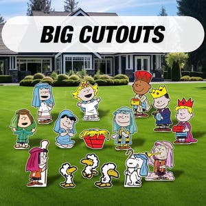 May include: Colorful outdoor yard decorations featuring cartoon characters, including figures with crowns, robes, and halos, and the text "BIG CUTOUTS" in a white banner. The decorations are placed on a green lawn in front of a house.