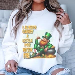 May include: White sweatshirt with a green leprechaun cartoon wearing a green hat and holding a pipe. The leprechaun is sitting on a pile of gold coins next to a pot of gold. The text on the shirt reads "I always carry a little pot with me".