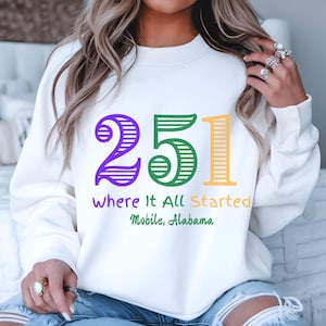 May include: White sweatshirt with a purple, green, and yellow striped design that says "251 Where It All Started Mobile, Alabama".