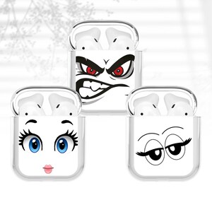 May include: Three clear protective cases for wireless earbuds, each with a different cartoon face design. One case has an angry face with red eyes, another has a face with blue eyes and pink lips, and the third has a sleepy face.