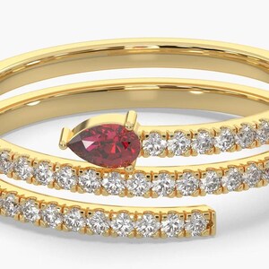 May include: A gold-colored spiral ring with a pear-shaped, deep red gemstone at the top. The ring is encrusted with small, clear gemstones along the spiral bands. The ring's design is elegant and modern.