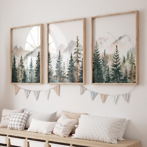 May include: Three framed watercolor paintings of a forest scene with mountains in the background. The paintings are in wooden frames and are hung on a white wall.