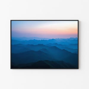 May include: A photograph of a mountain range at sunrise. The mountains are layered in shades of blue, with a pink and orange sky in the background.
