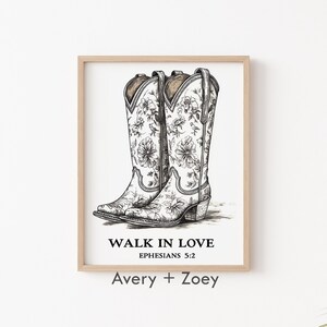 May include: A framed print with a black and white illustration of two cowboy boots with floral designs. The text "Walk in Love Ephesians 5:2" is below the boots. The names "Avery + Zoey" are printed below the text.