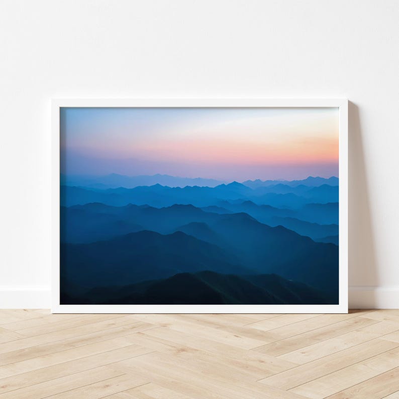 May include: A photograph of a mountain range at sunrise. The mountains are layered in shades of blue, with a pink and orange sky in the background.
