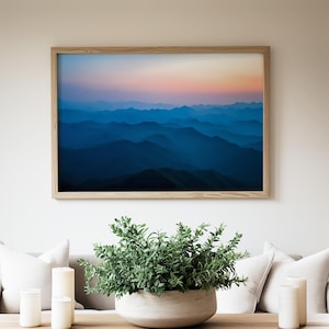 May include: A framed photograph of a mountain range at sunset. The mountains are a deep blue color and the sky is a soft pink and orange.