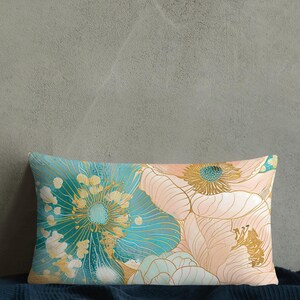 Op de afbeelding: Een rechthoekig kussen met een bloemenpatroon met grote, gestileerde bloemen in tinten turquoise, perzik en goud. Het kussen ligt op een donkerblauwe bedsprei.