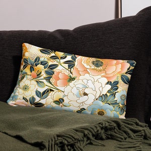 Op de afbeelding: Een decoratief kussen met een bloemenpatroon met witte, perzikkleurige en blauwe bloemen op een crèmekleurige achtergrond. De bloemen zijn omrand met goud en hebben een Japans geïnspireerd ontwerp.