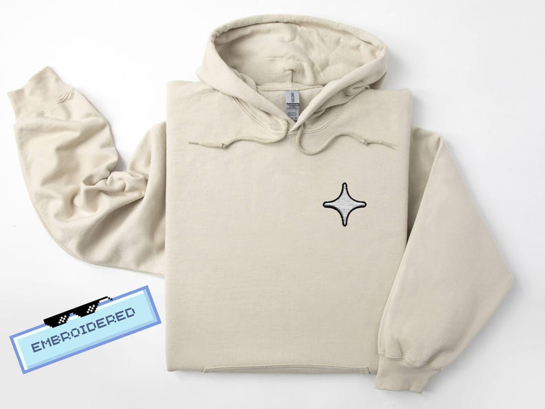 Puede incluir: Sudadera con capucha beige con capucha y cord&oacute;n. La sudadera presenta un peque&ntilde;o dise&ntilde;o de estrella bordada en la parte delantera. La palabra "EMBROIDERED" se muestra en una pancarta pixelada azul. La sudadera est&aacute; hecha de un material suave.