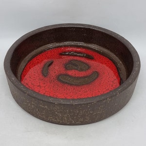 Può includere: Un piatto rotondo in ceramica con un esterno marrone e un interno rosso. L'interno rosso presenta un design a spirale marrone.