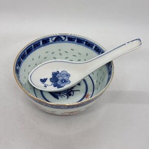 May include: A white porcelain bowl with a blue and white floral design and a matching blue and white porcelain spoon. The bowl has a scalloped edge and a small hole in the bottom.