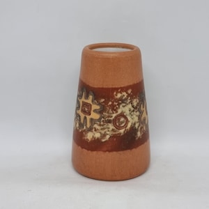 May include: A terracotta-colored vase with a flared shape. The vase features a band of dark brown and cream-colored abstract designs around the middle. The top and bottom sections are a solid terracotta color. The interior is white.