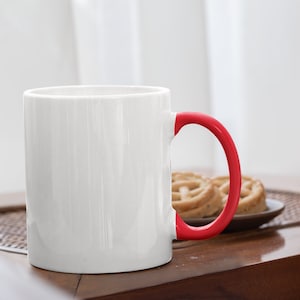 May include: White ceramic mug with a red handle. The mug is sitting on a wooden table.