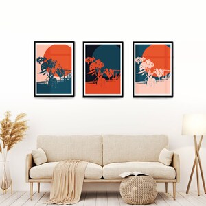 May include: Three framed prints with a minimalist design featuring a stylised plant with a large orange circle behind it. The prints have black frames and are displayed on a white wall above a beige sofa.