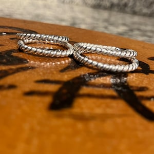 May include: Three silver rings with a twisted rope design. The rings are stacked on top of each other.