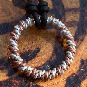 May include: A silver and copper twisted wire ring pendant on a black leather cord. The pendant is a simple circle shape.