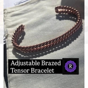 May include: A copper-colored metal cuff bracelet featuring a twisted, rope-like design. The bracelet is open-ended and adjustable. A black rectangular label at the bottom displays the white text Adjustable Brazed Tensor Bracelet and a purple logo.