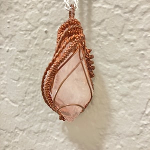 May include: A pink crystal pendant wrapped in copper wire, hanging from a silver chain.
